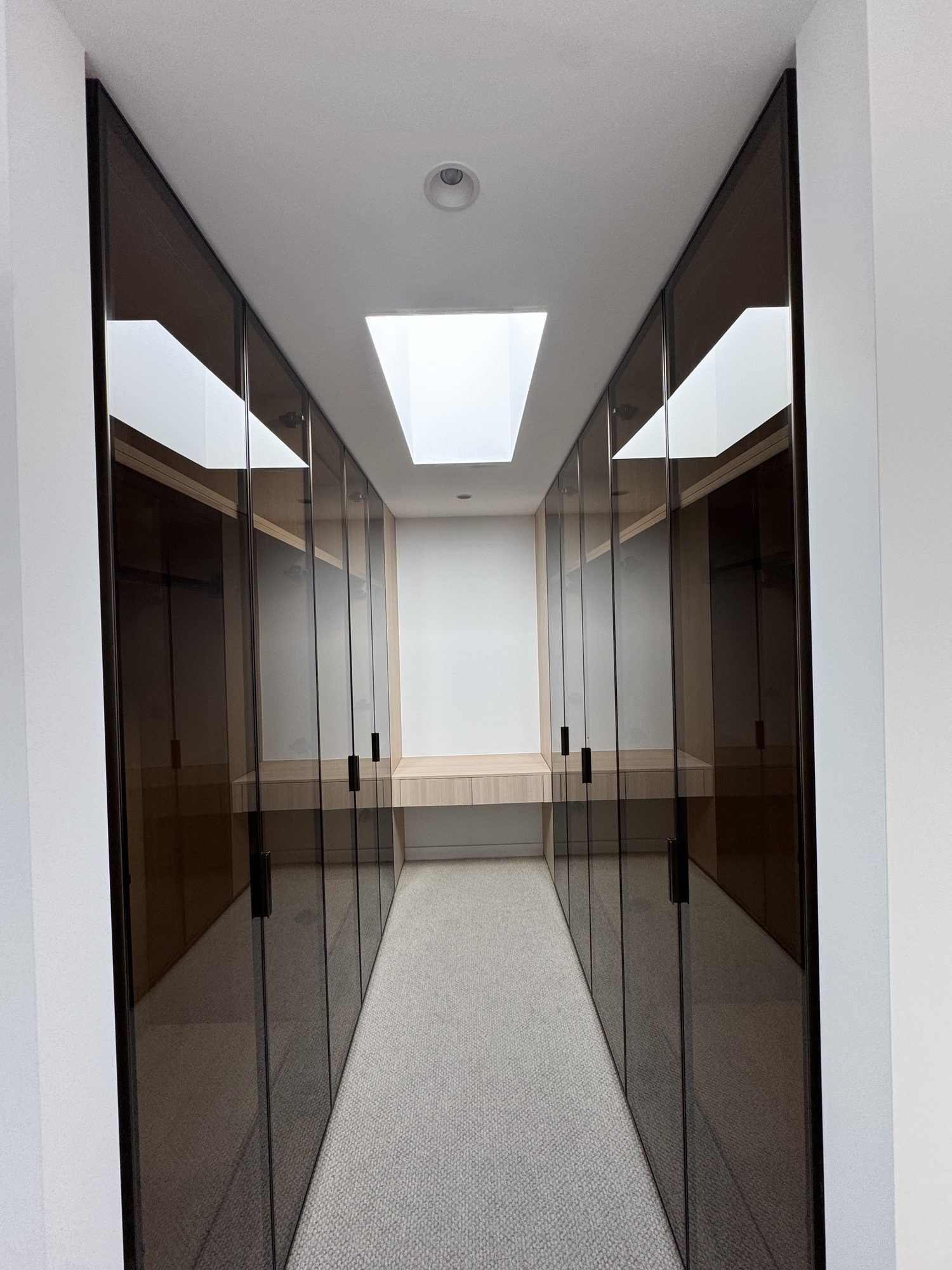 Dressing room lined with mirrored joinery under a skylight