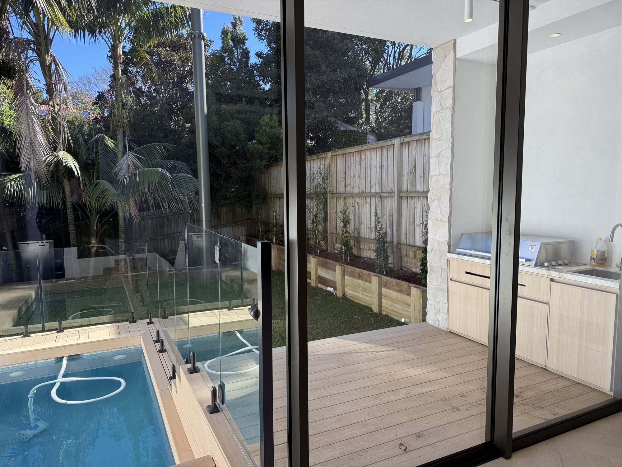 Living room opening through full-height glazing to the deck and pool