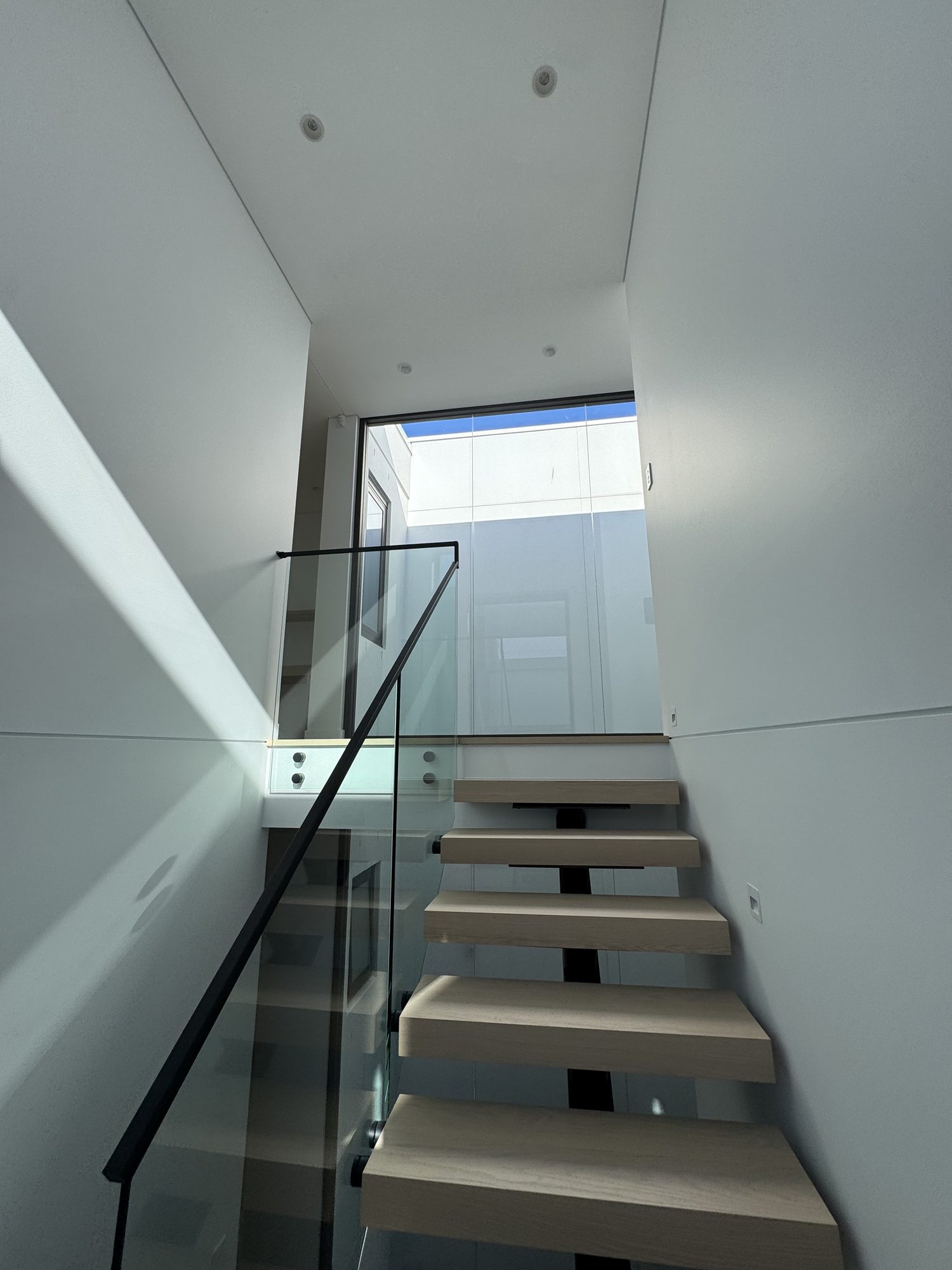 Stair with floating timber treads and a glass balustrade under a skylight